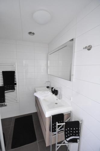 a white bathroom with a sink and two chairs at Roosjesweg 1a in Domburg