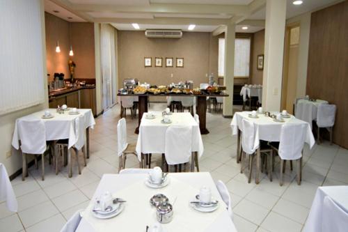 uma sala de jantar com mesas brancas e cadeiras brancas em Hotel 2 Gauchos em Naviraí