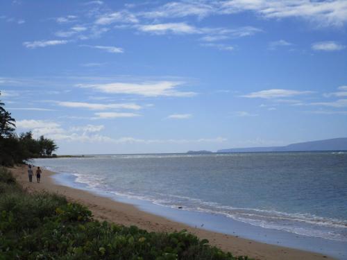 a beach with two people walking on the sand at Kauhale Makai Condo on the Beach in Kihei