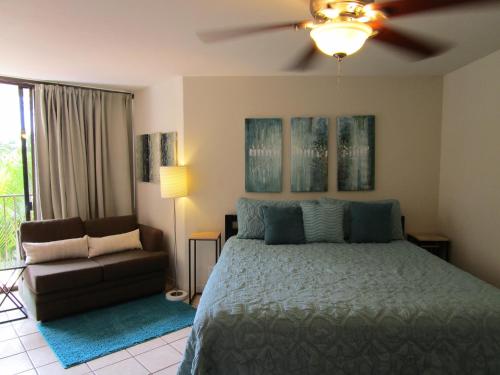 a bedroom with a bed and a couch and a ceiling fan at Kauhale Makai Condo on the Beach in Kihei