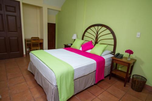 a bedroom with a large bed with pink and green sheets at Hotel Colibri in Managua