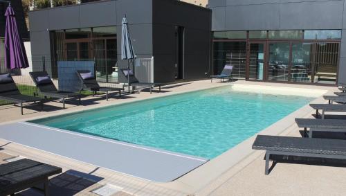 une grande piscine avec des chaises et un bâtiment dans l'établissement Logis Chez Camillou, à Aumont-Aubrac