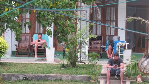 two men sitting on benches in a yard with their cell phones at Turtle Bay Beach Resort in Mirissa