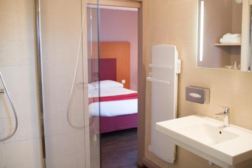 a bathroom with a sink and a shower with a bed at The Originals City, Hôtel Le Sextant, Toulouse Sud in Labège