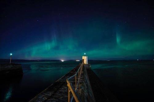 a pier with a light house and the northern lights at Mulberry in Nairn