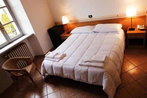 a bedroom with a large white bed and a chair at Hotel Portici in Vicoforte