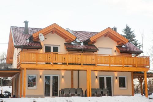 a house with a wooden deck in the snow at Ferienhäuser Glück Auf, Sauna, Hottubs in Arnoldstein