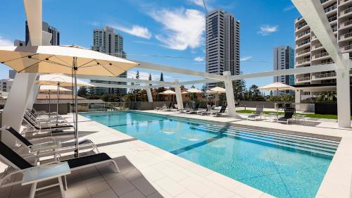 una piscina con sillas y sombrillas en un edificio en Avani Broadbeach Residences en Gold Coast