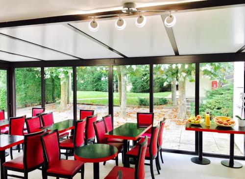 un restaurant avec des chaises rouges, des tables et des fenêtres dans l'établissement Hotel Pavillon des Gatines, à Plaisir