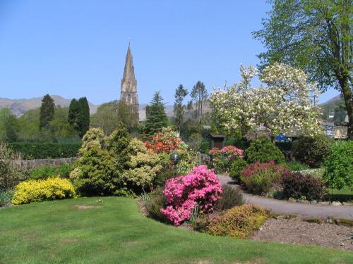 a garden with flowers and a church in the background at Rothay Garth in Ambleside