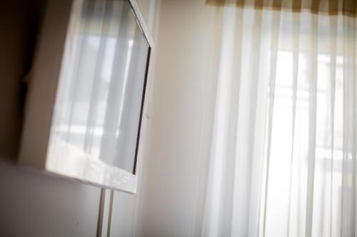 a window with a white curtain and a mirror at Il Portico Camere e Caffè - centro Città in Savignano sul Rubicone