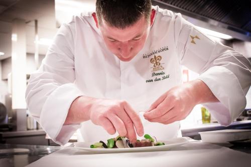 a chef preparing food on a plate in a kitchen at Relais & Chateaux Hotel Landgoed Het Roode Koper in Ermelo