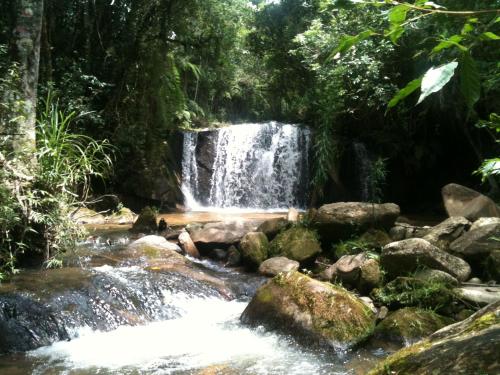 a waterfall in the jungle with rocks and trees at Delirius Hospedagem in Itamonte