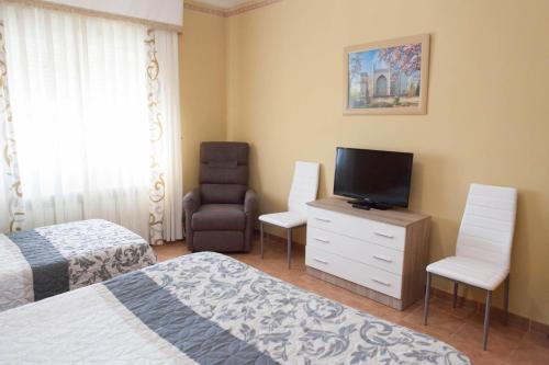 a bedroom with two beds and a television and a chair at La Rosaleda de Orgaz in Orgaz