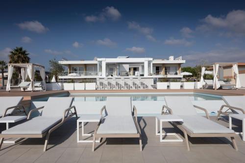 a swimming pool with white chairs and a house at Mercure Villeneuve Loubet Plage in Villeneuve-Loubet