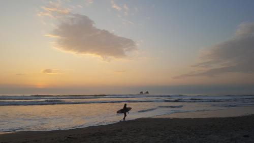a person walking on the beach with a surfboard at Las Cabañas de la Iguana in Ayampe