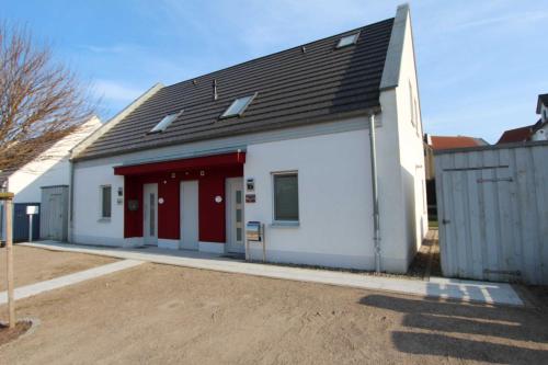 a white building with a black roof and red doors at Ferien_HAUS FOHLENWEIDE in Göhren-Lebbin