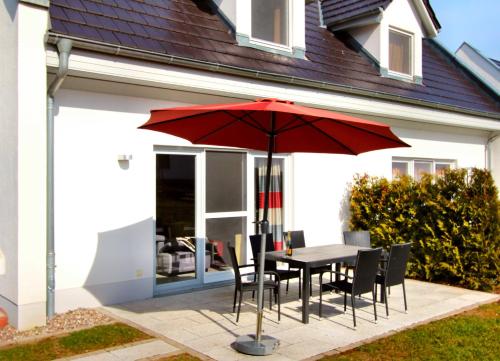 a table and chairs with a red umbrella in front of a house at Ferien_HAUS FOHLENWEIDE in Göhren-Lebbin