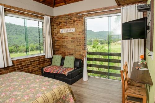 um quarto com uma cama, um sofá e uma janela grande em Bina's Haus Pousada, Cafeteria e Atelier em Nova Petrópolis