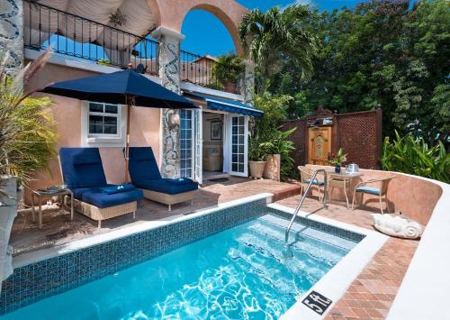 a pool with chairs and an umbrella next to a house at Little Arches Boutique Hotel - Adults Only in Christ Church
