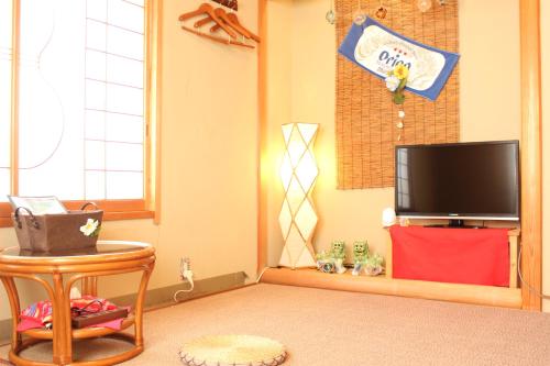 a living room with a flat screen tv and a table at Okinawa Minshuku Kariyushi in Shirahama