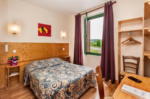 Schlafzimmer mit einem Bett, einem Tisch und einem Fenster in der Unterkunft Hotel de France in Chaudeyrac