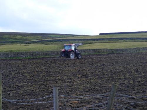 a tractor is plowing a field behind a fence at The Dog and Partridge in Langsett