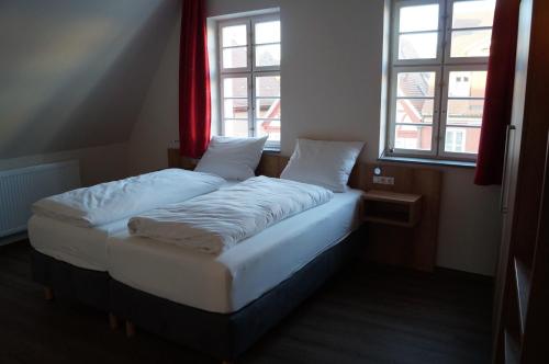 a twin bed in a room with two windows at Braumeister Döbler - Ferienwohnungen in Bad Windsheim