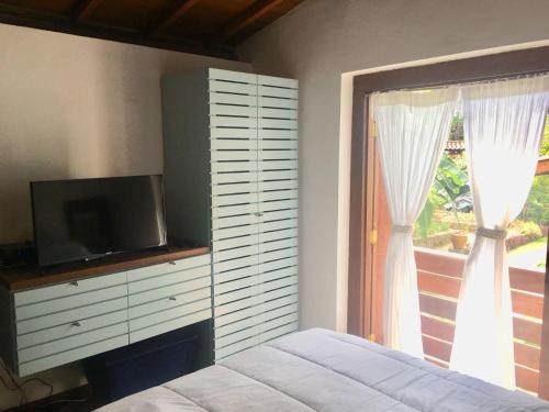 um quarto com uma cama, uma televisão e uma janela em Casa pé na areia - Praia do Felix em Ubatuba