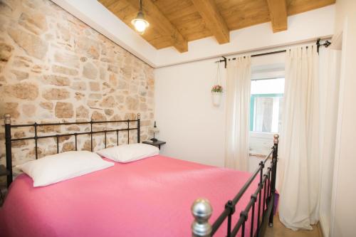 a bedroom with a pink bed and a stone wall at Apartments Nove Crkve in Šibenik