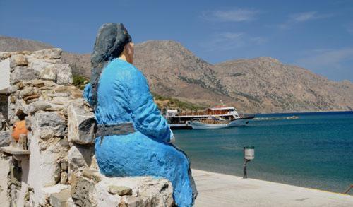 a statue of a woman sitting on a wall near the water at Dorana Apartments & Trekking Hotel in Diafani