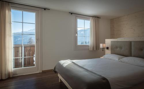 a bedroom with a bed and two windows with mountains at Hotel Villa Argentina in Cortina dʼAmpezzo