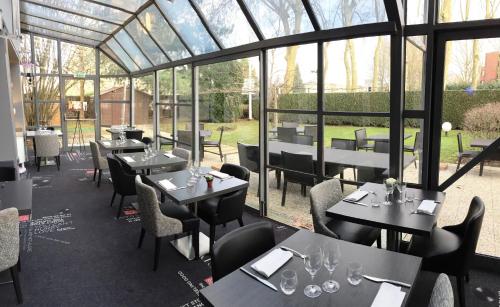 a restaurant with tables and chairs and glass windows at Best Western Paris Saint Quentin in Montigny-le-Bretonneux