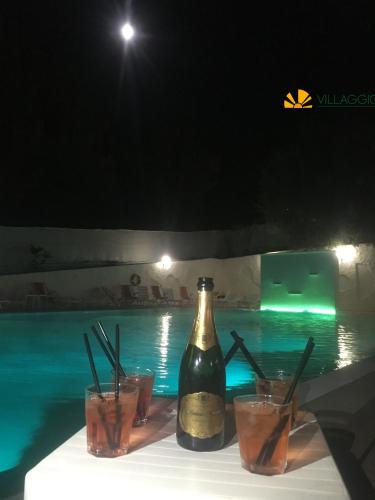 a bottle of wine and glasses next to a swimming pool at Villaggio Elisena in Vieste