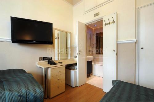 a bedroom with a desk and a tv on the wall at Rhodes Hotel in London