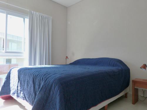 Un dormitorio con una cama azul y una ventana en Apartamentos Valeria Medanos en Valeria del Mar