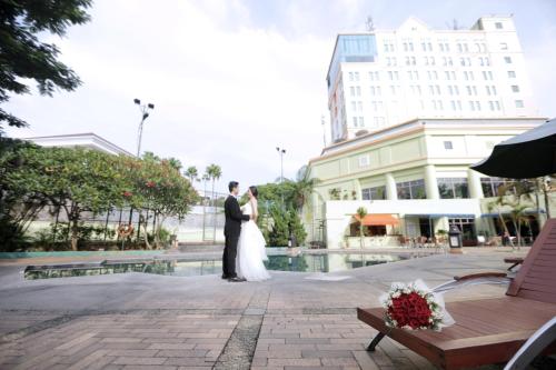 a bride and groom standing in front of a pool at Grand Candi Hotel in Semarang