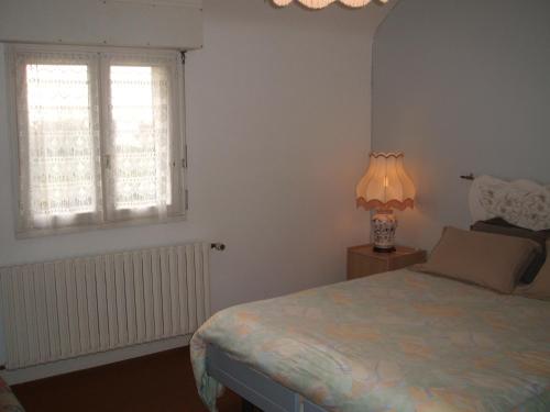 a bedroom with a bed and a lamp and a window at Maison Lallier in Plonevez-Porzay