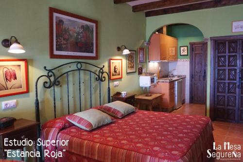 a bedroom with a red bed and a kitchen at La Mesa Segureña in Segura de la Sierra