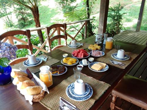 una mesa con alimentos para el desayuno y zumo de naranja en ella en Pousada das Fadas, en Visconde De Maua