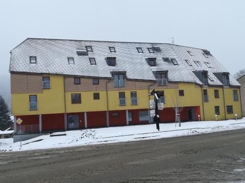 a large yellow and red building on a snowy street at Apartmán Deštná čp.1 in Deštné v Orlických horách