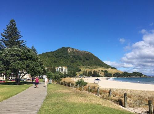 people walking down a sidewalk next to a beach at Victoria Road B&B in Mount Maunganui
