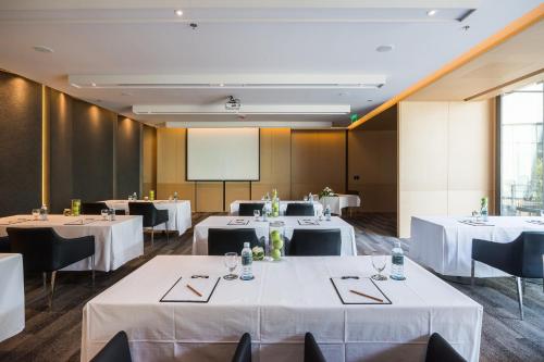 Una sala de conferencias con mesas y sillas blancas y una pantalla. en Arize Hotel Sri Racha, en Si Racha