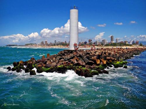 a lighthouse on a rock formation in the water with a beach at Pousada Recanto da Prainha in Torres
