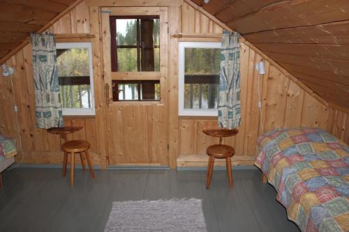 a bedroom in a log cabin with a bed and two windows at Mäkitorppa in Varpaisjärvi