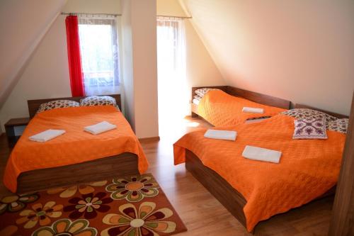 two beds in a small room with orange sheets at Pokoje Gościnne Hosana in Poronin