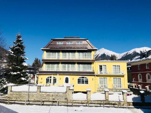 a yellow house with mountains in the background at Hotel Lindenhof in Bad Gastein