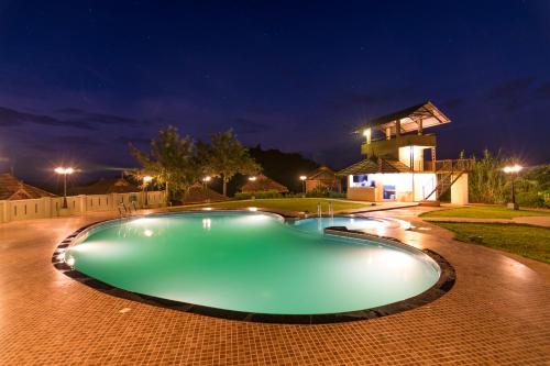 een zwembad 's nachts met een huis op de achtergrond bij Wayanad Village Resort in Koroth