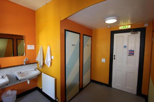 baño con paredes de color naranja, lavabo y espejo en Pitlochry Backpackers en Pitlochry