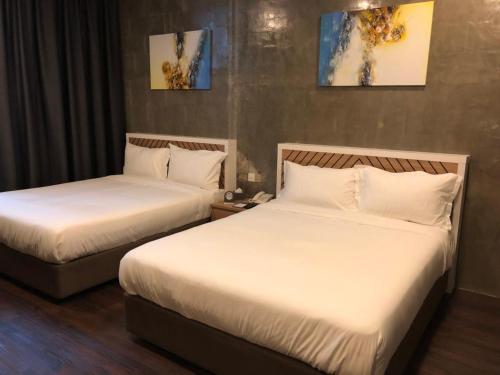 two beds in a hotel room with white sheets at K Boutique Hotel in Teluk Intan